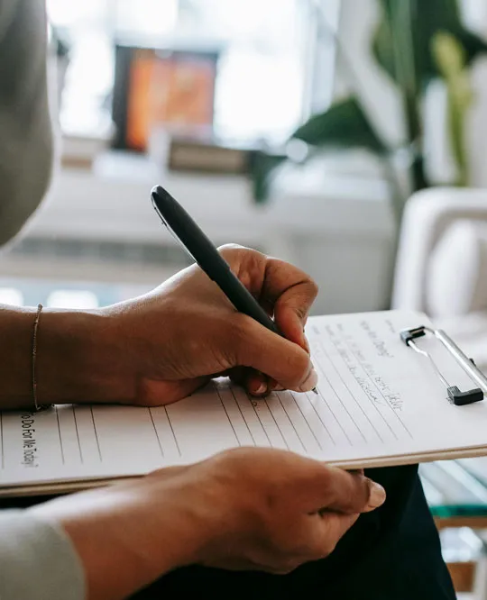 Una persona escribiendo en un cuaderno sobre una mesa con elementos de oficina.