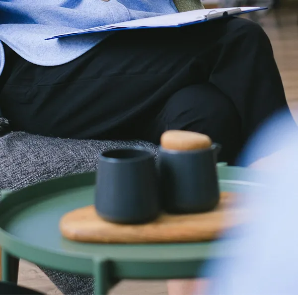 Una persona sentada en un sofá con dos tazas de café sobre una mesa pequeña.